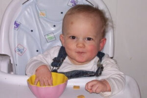 mischievous looking baby eating Cheerios in a high chair