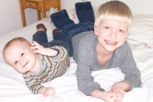 a little boy and a baby lying on their stomachs smiling